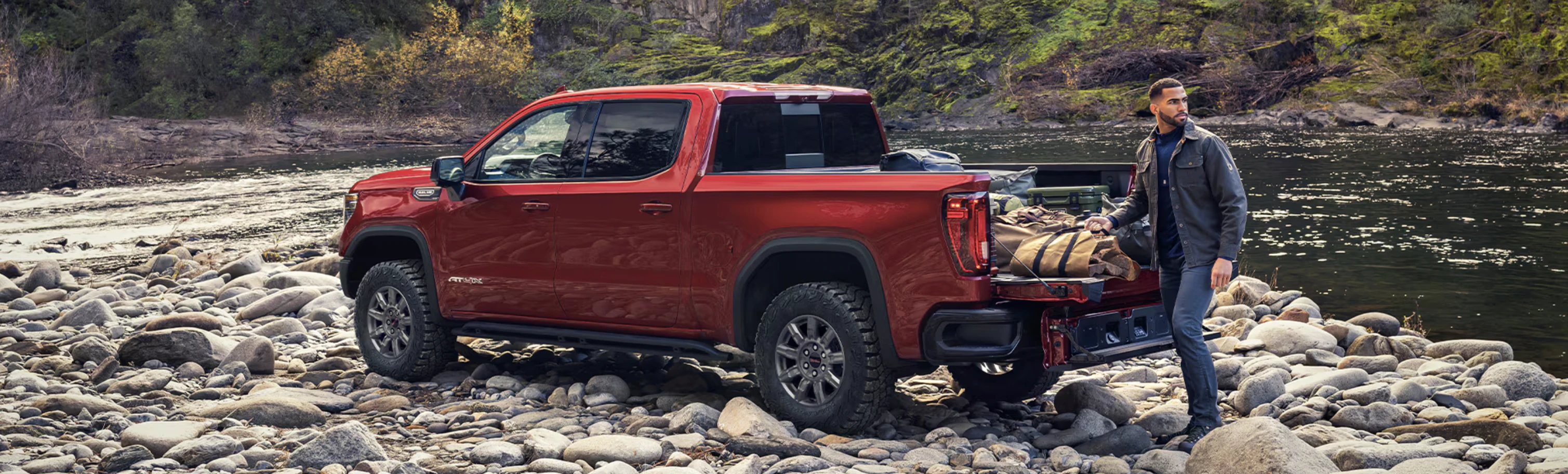 Rear side view of GMC Sierra parked on rocks with man taking gear out of the box