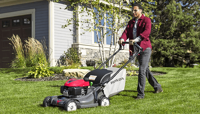 A man using a self-propelled Honda mower in his front yard
