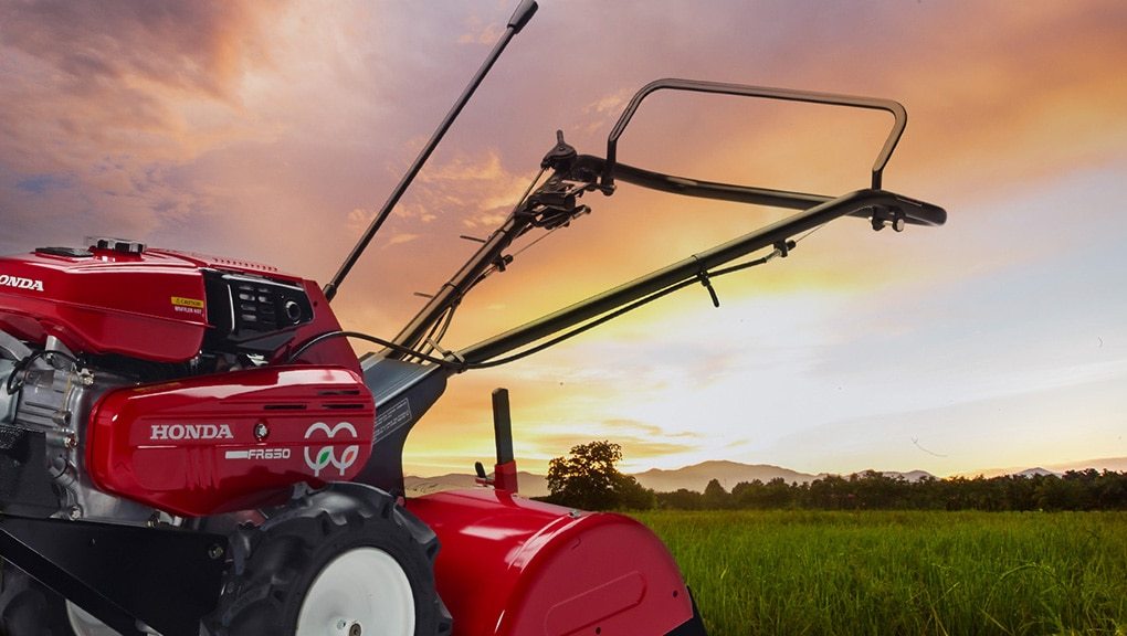 Honda tiller in the foreground with a field and the sun setting in the background