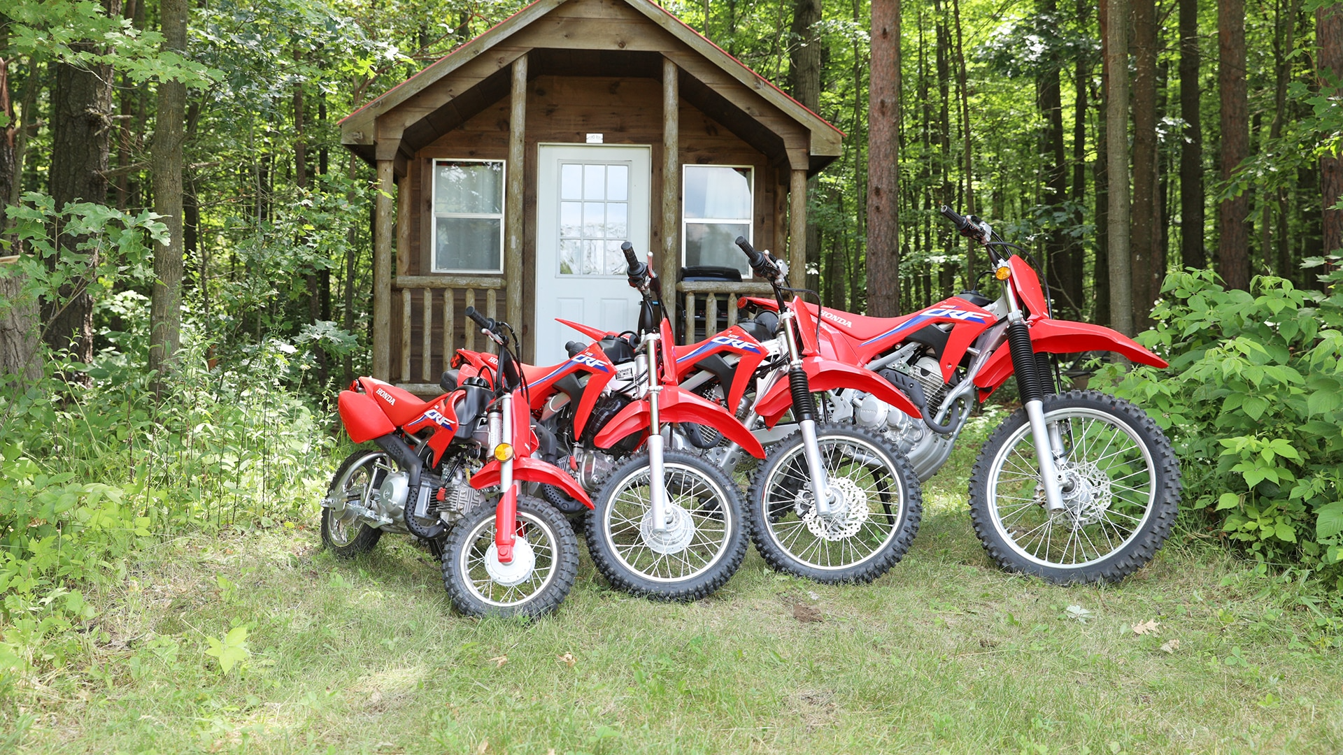 Line of CRF125F bikes in front of a cabin