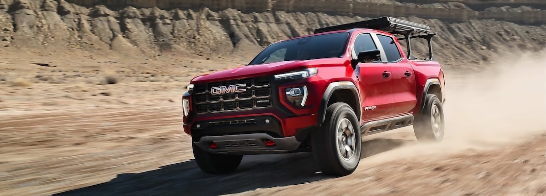 A red 2026 GMC Canyon AT4 drives on sand.