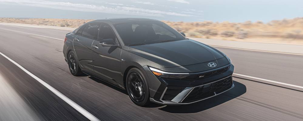 A black 2026 Hyundai Elantra drives along a road. New 2026 Hyundai Elantra performance specs at Gus Brown Hyundai in Brooklin, ON