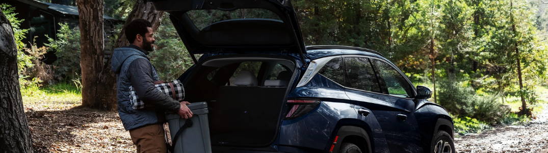 A man loading cargo into a 2025 Tucson PHEV parked in a forest