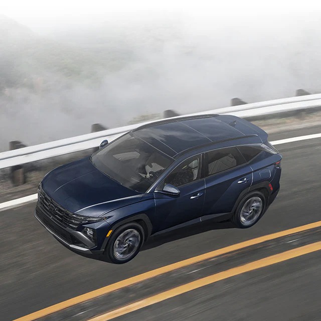 A black 2026 Hyundai Tucson drives along a mountain road. New 2026 Hyundai Tucson for sale at Gus Brown Hyundai