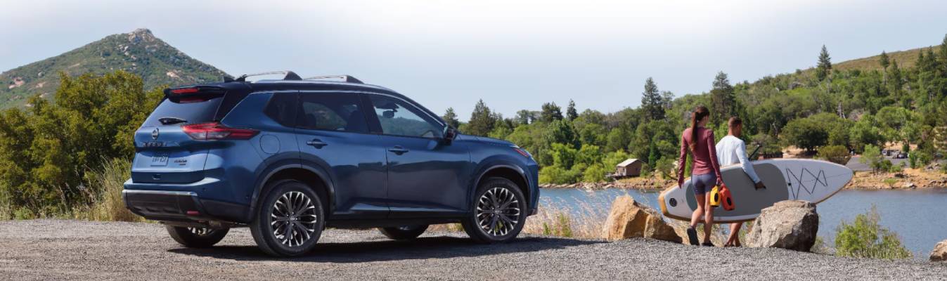 A deep blue 2026 Nissan Rogue is parked on the bank near a lake where people are gathered to have fun