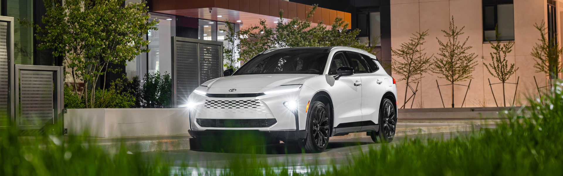 Front three-quarter view of a white Toyota Crown Signia parked outdoors at night with headlights on
