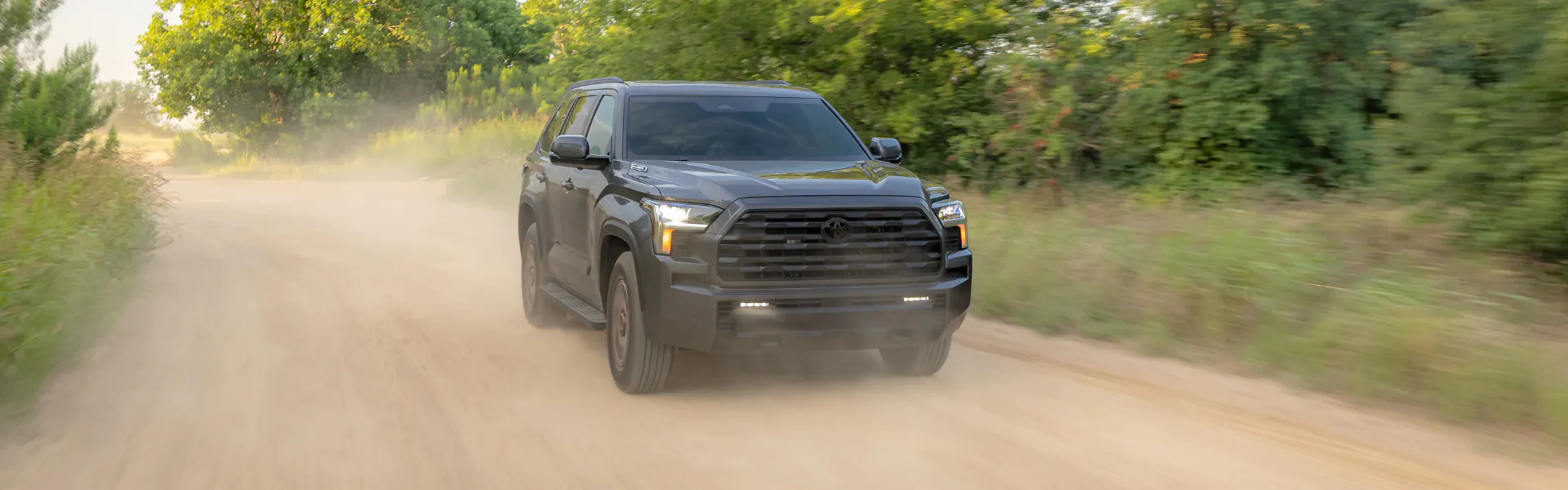 Toyota Sequoia driving on a dusty dirt road through a wooded area
