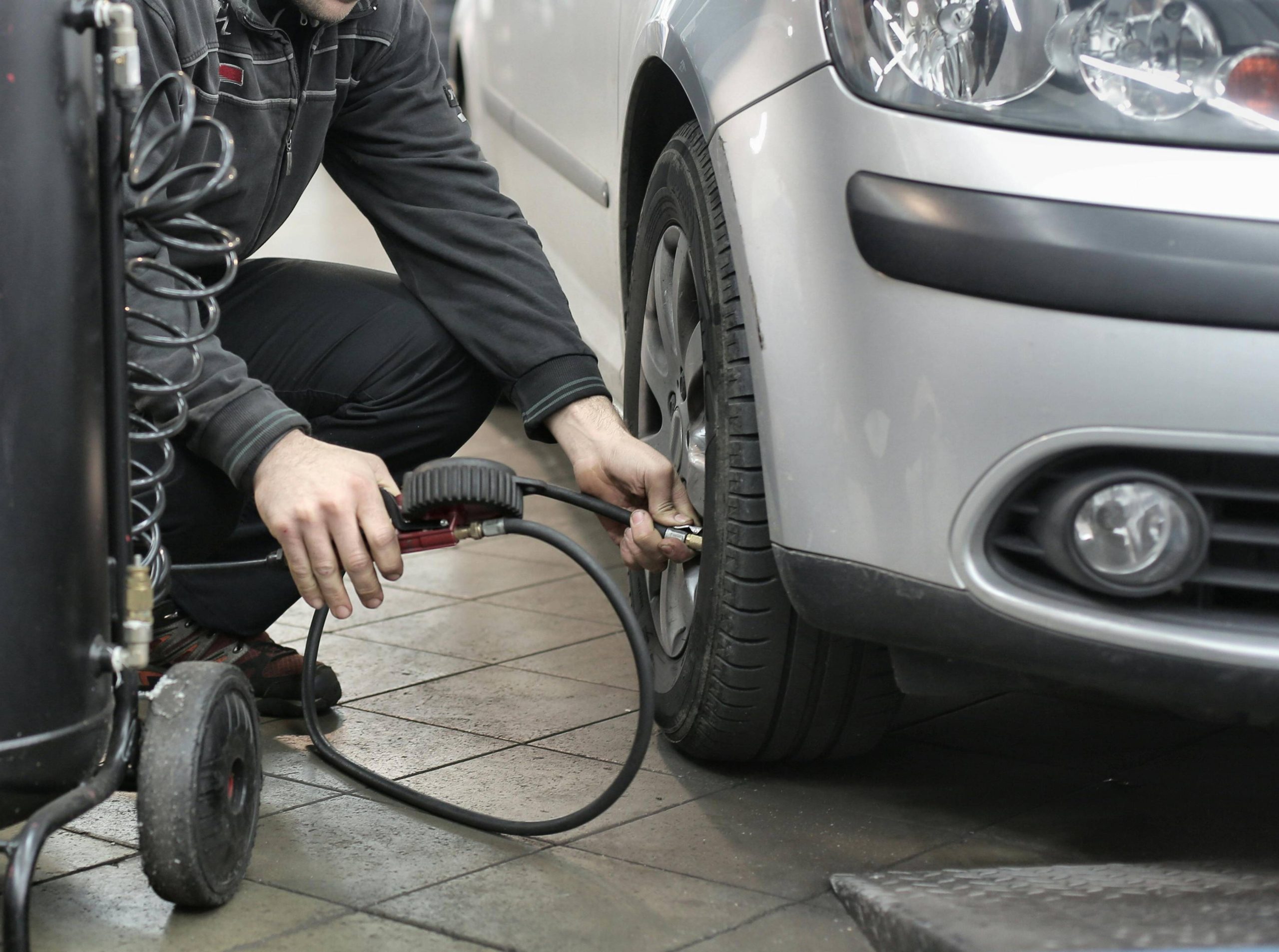 A technician dressed in black inflates a white car's tire
