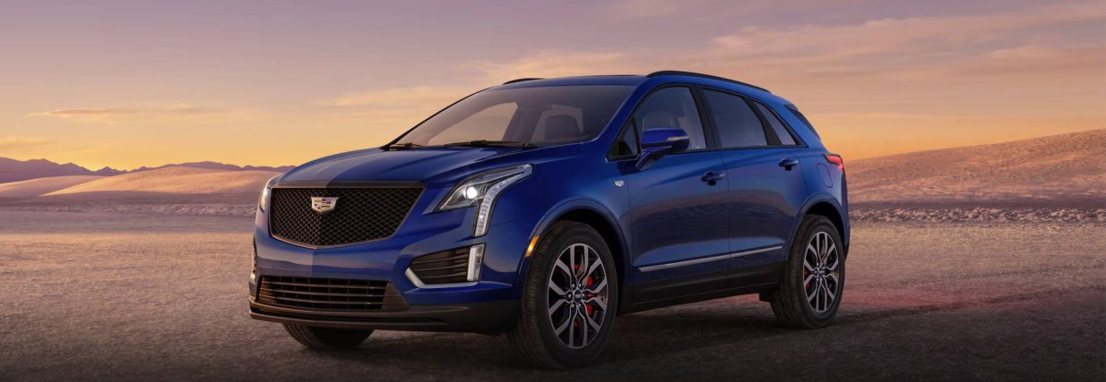 A blue 2025 Cadillac XT5 sits in front of a sunset