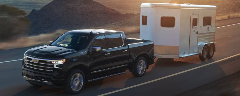 A black 2026 Chevrolet Silverado 1500 pulls a white trailer along a road surrounded by hilly dirt terrain. New 2026 Chevrolet Silverado 1500 for sale in Yorkton, SK at FFUN Chevrolet Buick GMC