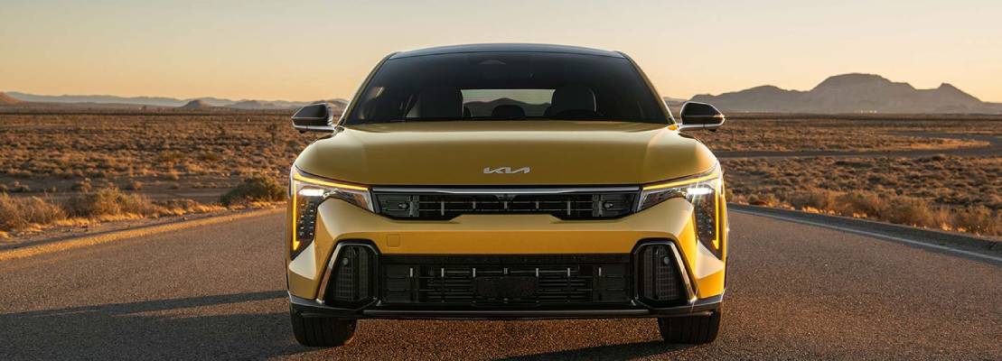 A yellow 2026 Kia K4 Hatchback faces the camera head-on in front of a setting sun