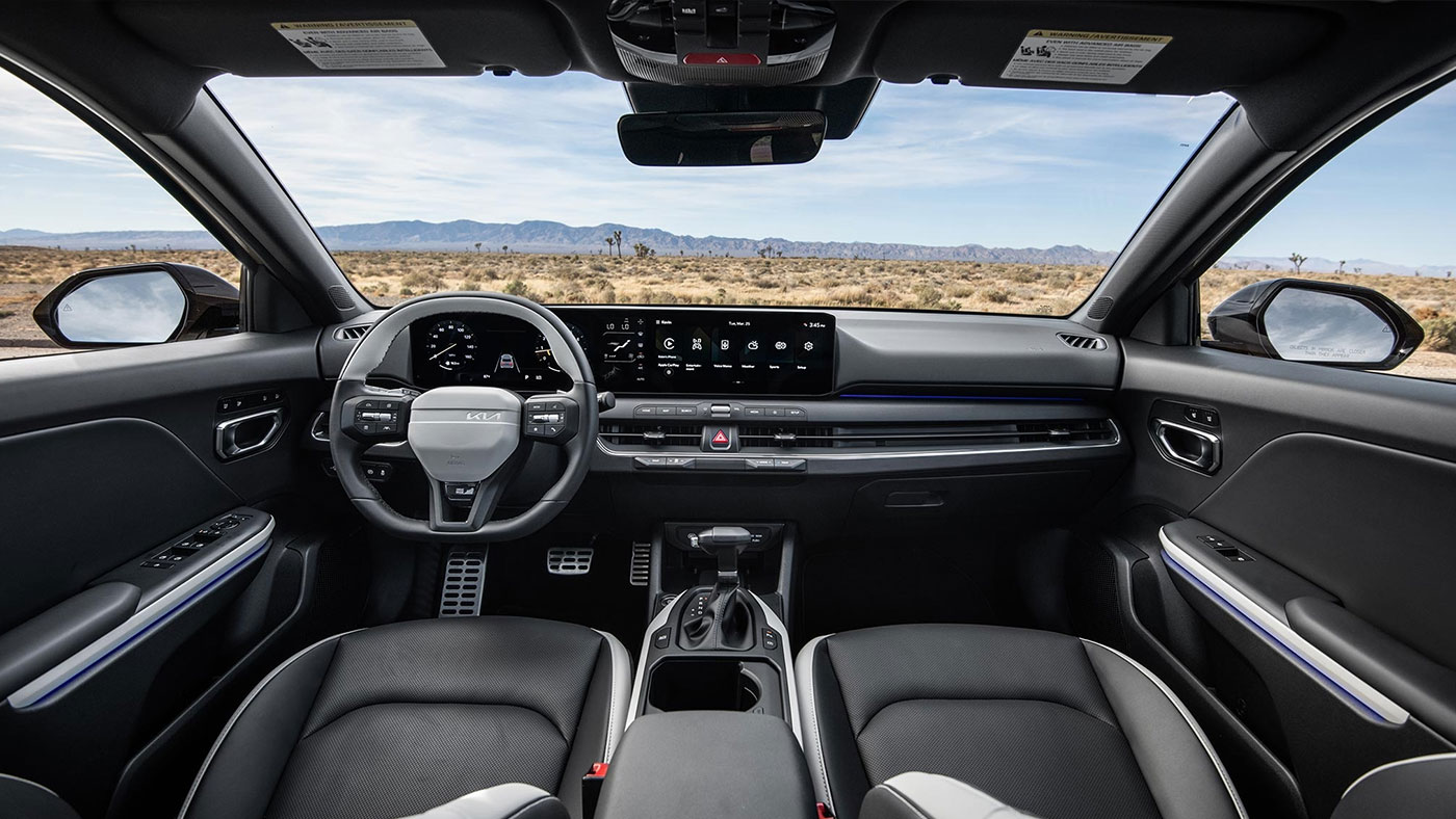 The front row seats and dashboard of the 2026 Kia K4 Hatchback, with blue skies beyond the windows