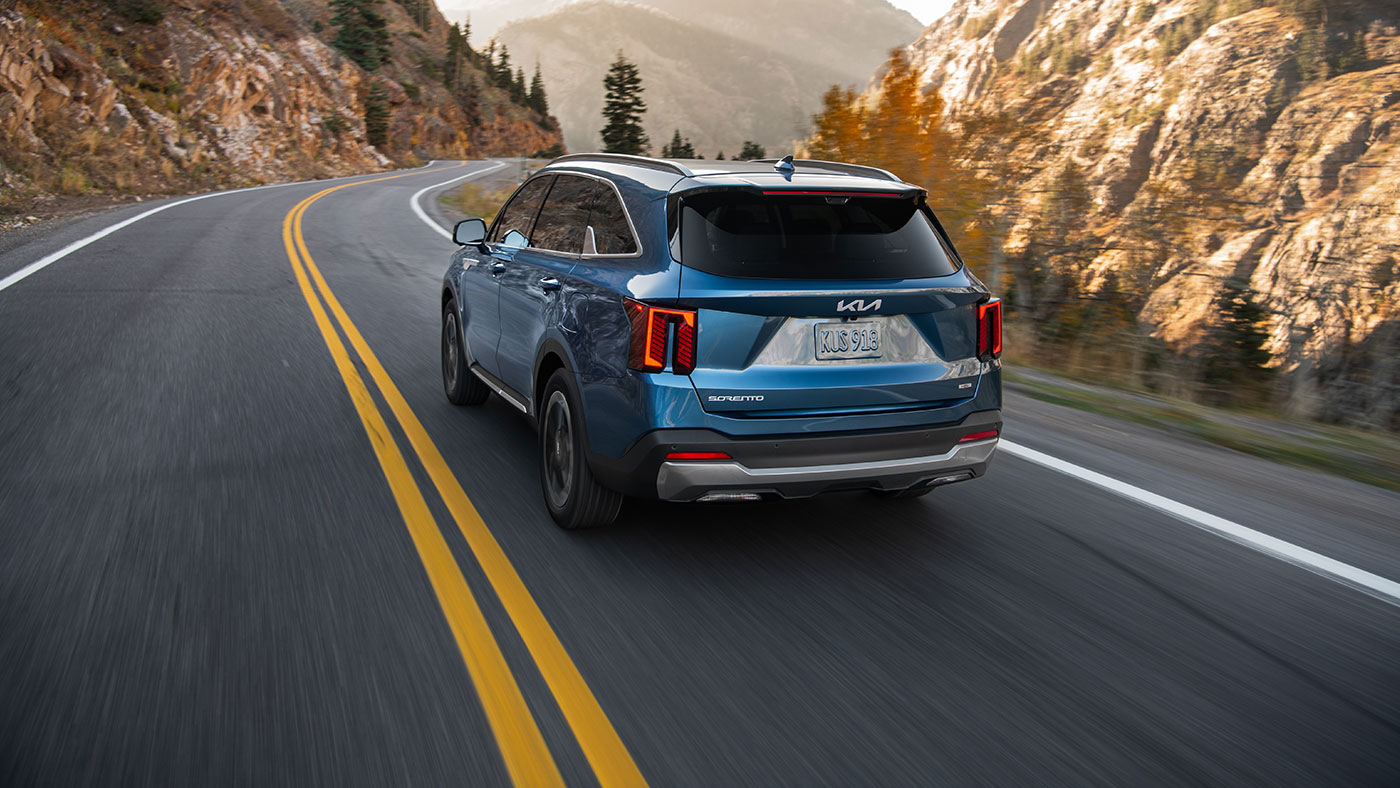 A blue 2026 Kia Sorento PHEV drives away from the camera with cliffs on either side of the road
