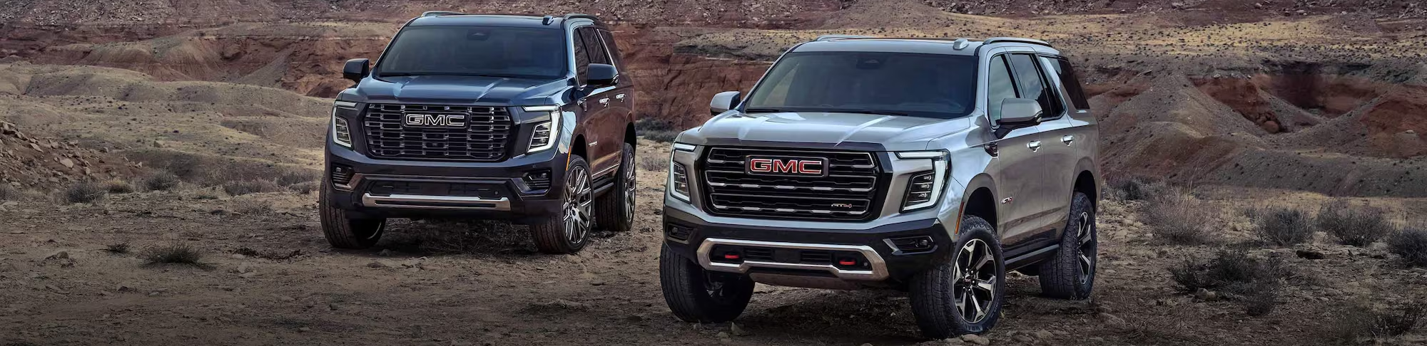 A 2025 GMC Yukon & Yukon XL are parked together on brown desert or prairie off-road land