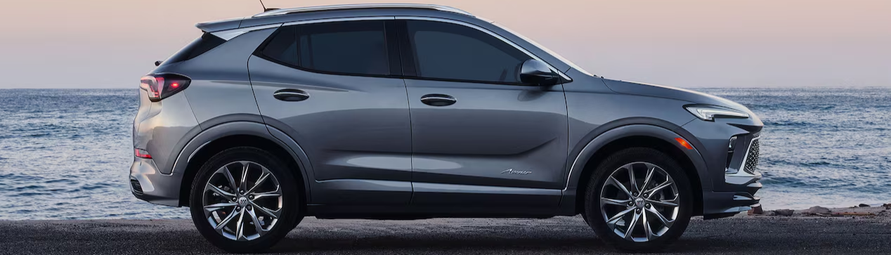 A side view of a silver 2026 Buick Encore GX in front of the ocean at sunset