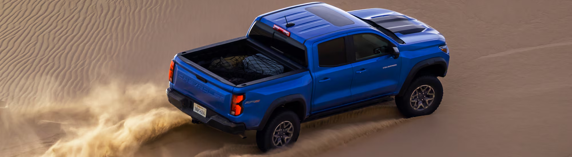 A blue 2026 Chevrolet Colorado drives across the desert, kicking up sand. New 2026 Chevrolet Colorado for sale at Laplante Chevrolet Buick GMC in Casselman, ON