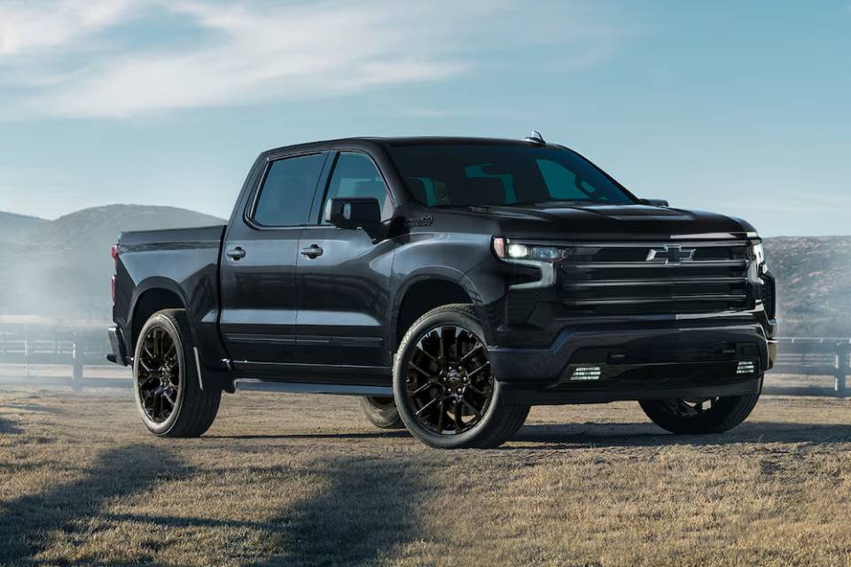 A black 2025 Chevrolet Silverado 1500 is angled on a ranch with blue skies above and the silhouette of a mountain range in the distance.