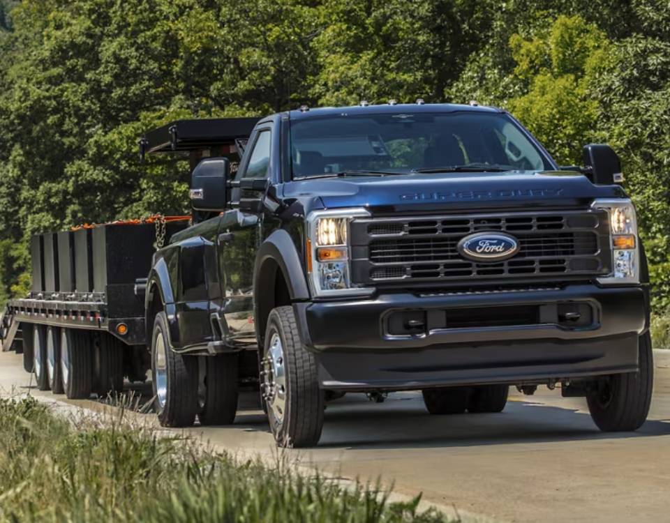 A 2025 Ford Super Duty HD truck pulls an industrial trailer along a bright green country road with forest in the background.