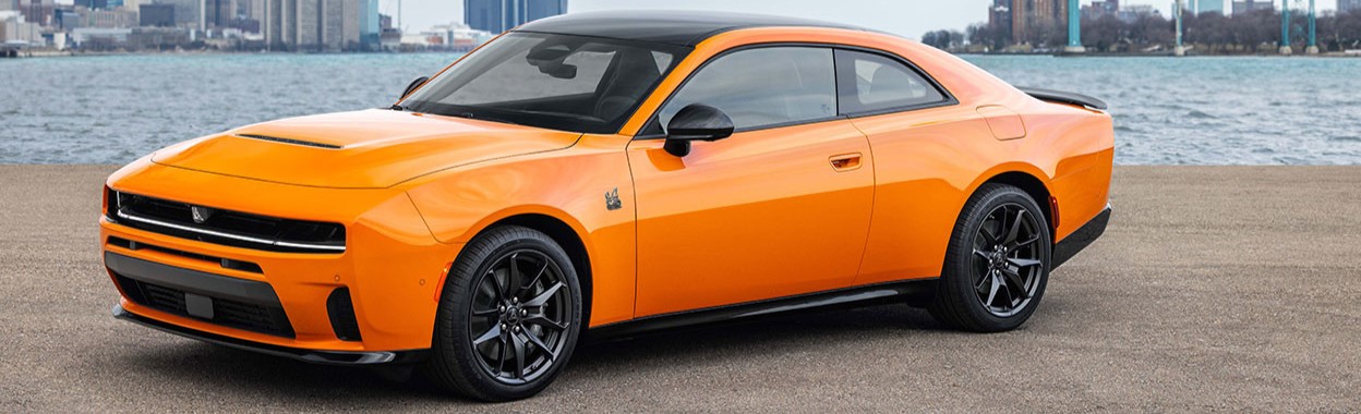An orange 2026 Dodge Charger sits on the bank of a port city with the harbour behind it