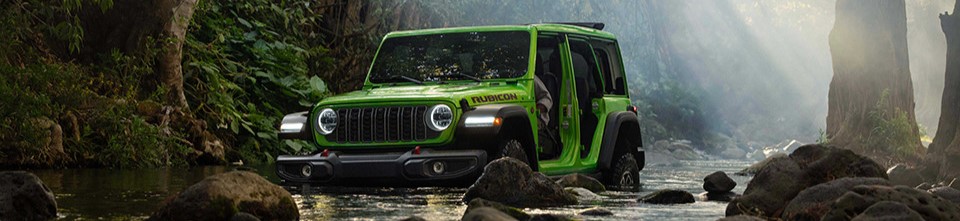 A green 2026 Jeep Wrangler drives through a forest