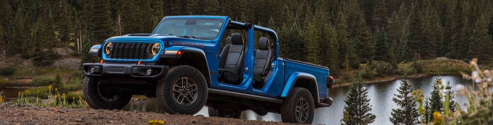 A blue 2026 Jeep Gladiator parked on a grassy incline with a lake in the background. New 2026 Jeep Gladiator for sale at Laplante Chrysler Dodge Jeep Ram in Embrun, ON