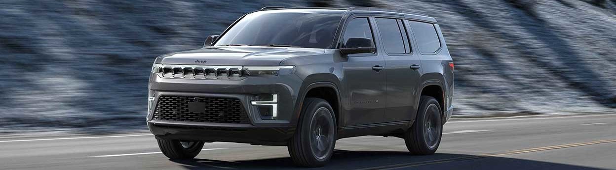 A 2026 Jeep Grand Wagoneer & L drives alongside a grey mountain slope. New 2026 Jeep Grand Wagoneer & L for sale at Laplante Chrysler Jeep Dodge Ram in Embrun, ON