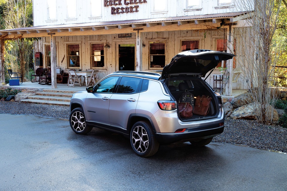 A silver 2025 Jeep Compass is parked outside of a cabin resort reception building with the trunk open