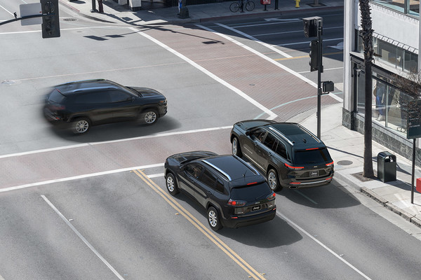 Two cars wait at an intersection while a third crosses traffic in front of them, demonstrating the 2025 Jeep Cherokee's Intersection Assist function