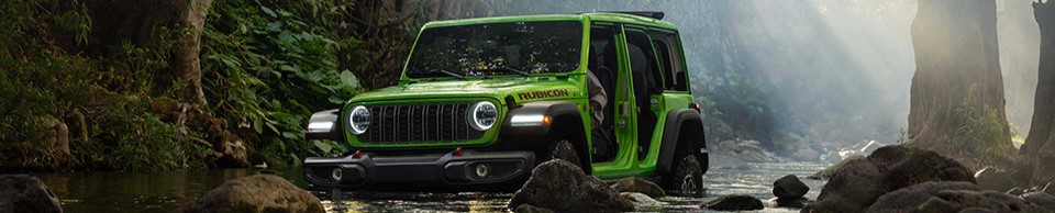 A green 2026 Jeep Wrangler drives through a forest