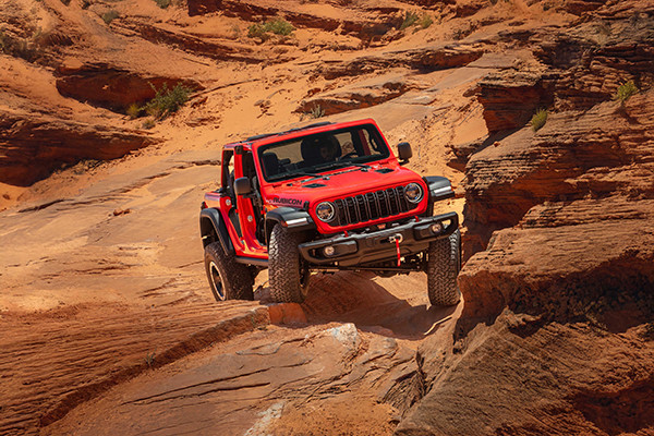 A red 2026 Jeep Wrangler navigates a tight, rocky mountain road. 2026 Jeep Wrangler performance specs at Leavens Chrysler Dodge Jeep Ram in London, ON