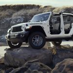 2026 Jeep Wrangler 85th Anniversary Edition in white with doors removed, parked on rocks in a coastal setting, promoted by Leavens Chrysler Dodge Jeep RAM London Ontario.