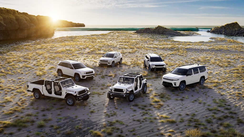Full 2026 Jeep SUV and truck lineup in white 85th Anniversary editions parked together on a sandy coastal plain, representing models available at Leavens Chrysler Dodge Jeep RAM London Ontario.