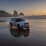 2026 Jeep Grand Cherokee L silver three‑row SUV driving along a reflective shoreline at sunset, featured by Leavens Chrysler Dodge Jeep RAM London Ontario.