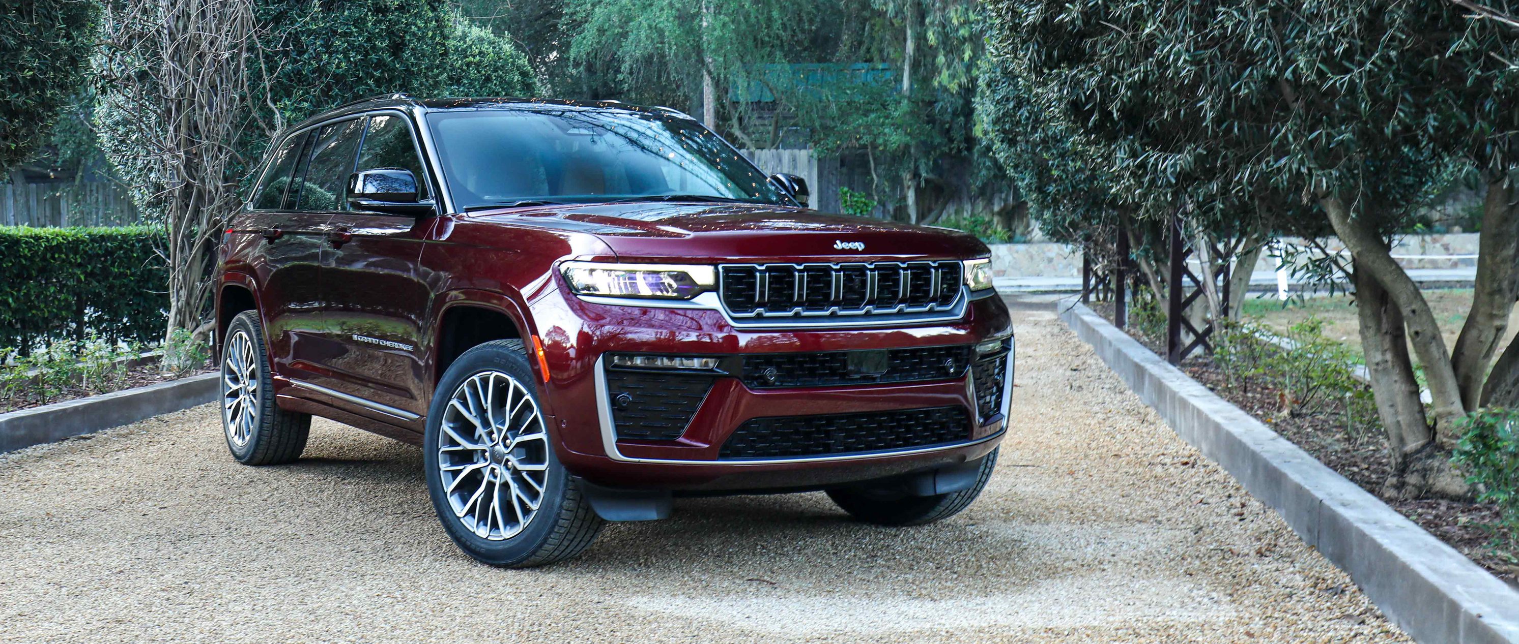 2026 Jeep Cherokee dark red SUV parked on a gravel drive surrounded by greenery and garden lights, showcased by Leavens Chrysler Dodge Jeep RAM London Ontario.