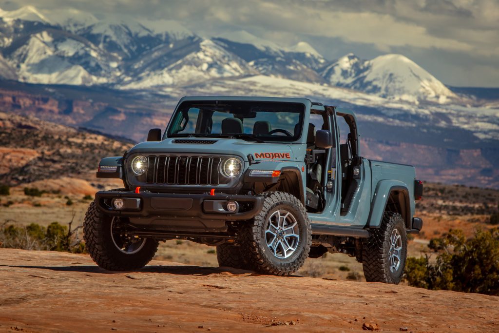 2026 Jeep Gladiator Mojave X pickup with open cabin parked on red rock with distant snow‑capped mountains, promotional photo for Leavens Chrysler London Ontario.
