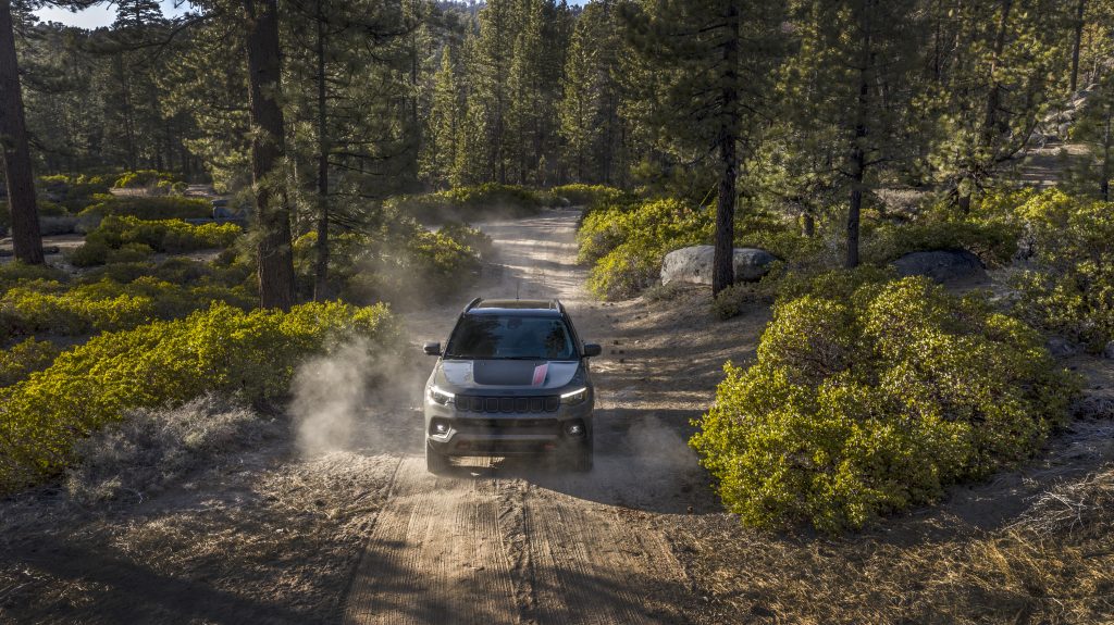 2026 Jeep Compass Trailhawk SUV driving on a dusty dirt road through a pine forest, front view used by Leavens Chrysler Dodge Jeep RAM London Ontario.