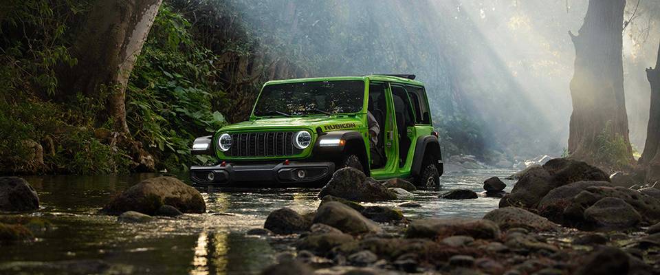A doorless 2026 Jeep Wrangler in Mojito! traverses a river in a forest. New 2026 Jeep Wrangler Design Features at Leavens Chrysler Dodge Jeep Ram in London, ON
