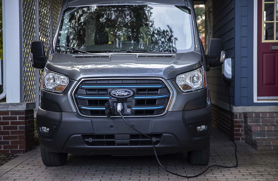 vue avant du Ford E-Transit 2022 stationné à côté d'une maison et branché à la borne électrique