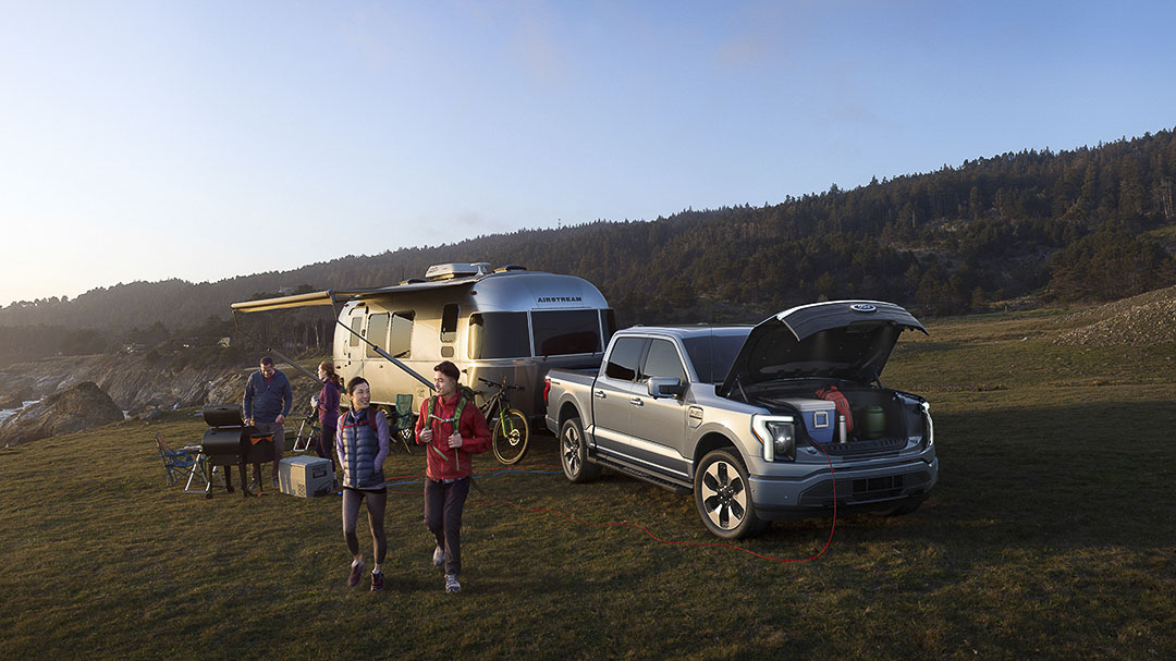 vue trois quart avant du Ford F-150 Lightning 2022 dans une plaine avwec une roulotte et son Frunk ouvert