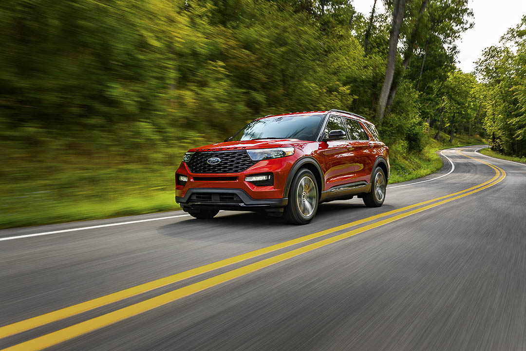 Le VUS Ford Explorer ST Line 2022 rouge roulant sur une route au bord d'une forêt