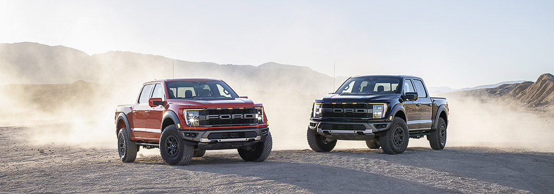 Deux camions Ford F-150 2021 de version Raptor garés côtes-à-côtes sur une terre de sable