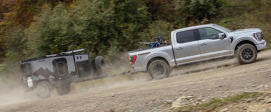 Vue latérale d'un camion Ford F-150 Tremor 2021 remorquant une mini-roulotte dans une côte de terre battue