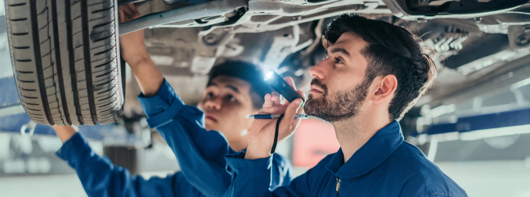 Two mechanics inspecting a car's wheel
