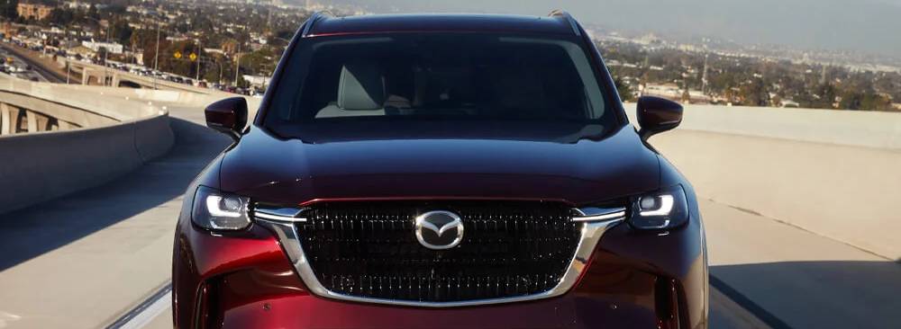A head-on view of a deep red 2025 Mazda CX-90 as it drives on a highway
