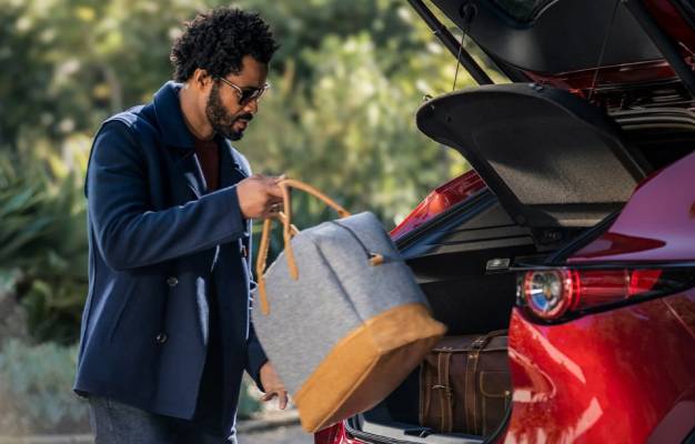 A man packs a grey and brown bag into the trunk of a red 2025 Mazda CX-30