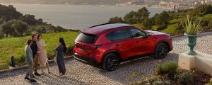 A red 2026 Mazda CX-5 sits on a cobblestone road with people socializing around it
