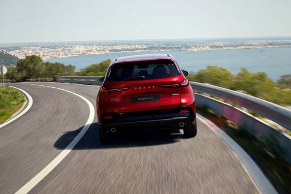 A red 2026 Mazda CX-5 speeds along a coastal highway