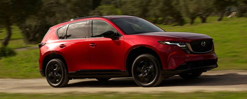 A red 2026 Mazda CX-5 drives past the camera in front of a green background