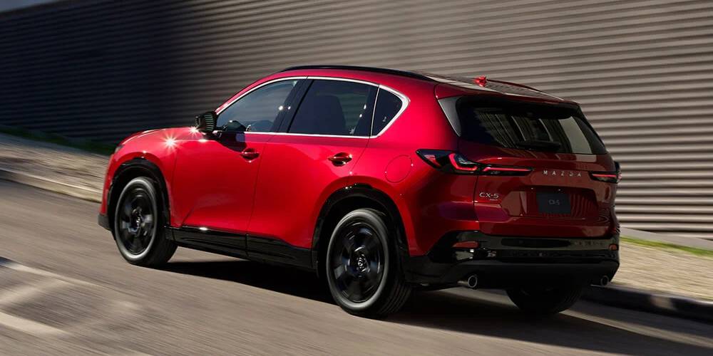 A red 2026 Mazda CX-5 drives uphill in an urban environment