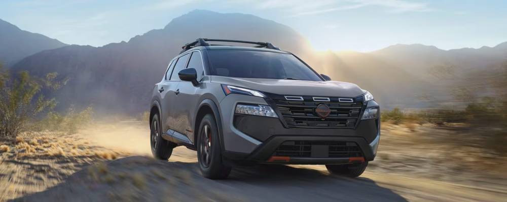 A 2026 Nissan Rogue drives over dirt road with mountains in the background